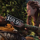 Aloy assists a bloody and wounded warrior leaning against a tree trunk in taking a drink of water from a gourd.